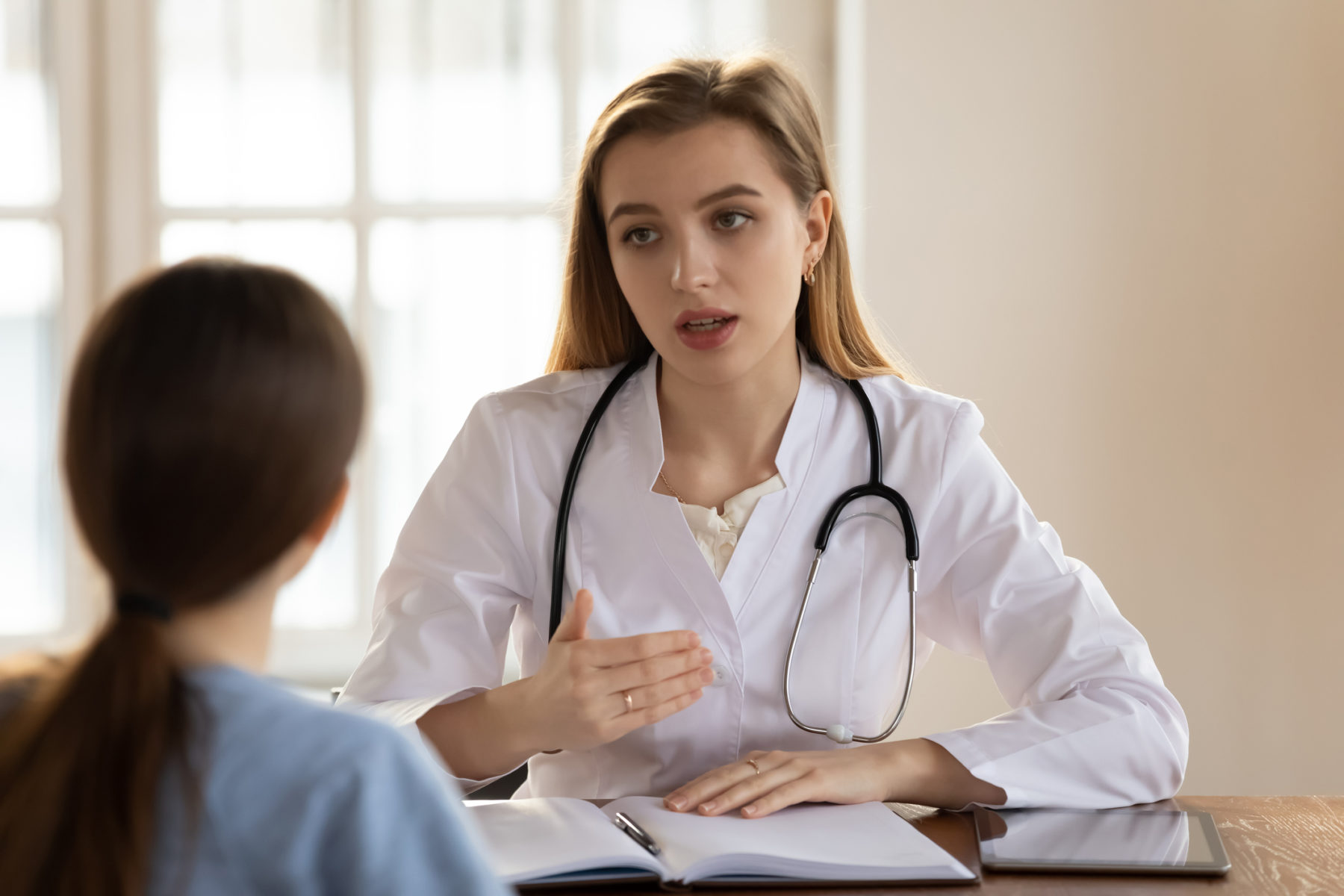Une jeune médecin explique quelque chose à une patiente assise en face d'elle, dans son cabinet