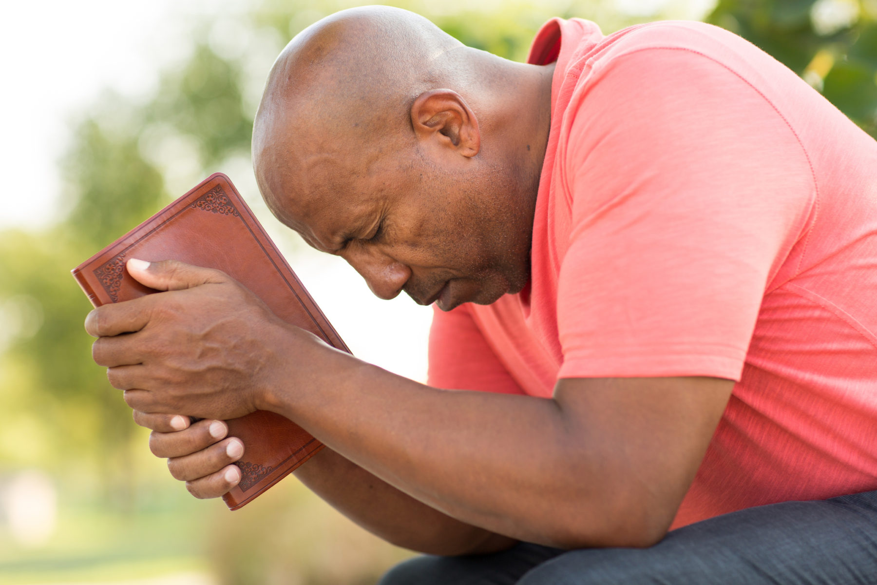 Un homme noir assis prie, le front appuyé sur la tranche d'une bible qu'il tient dans ses mains