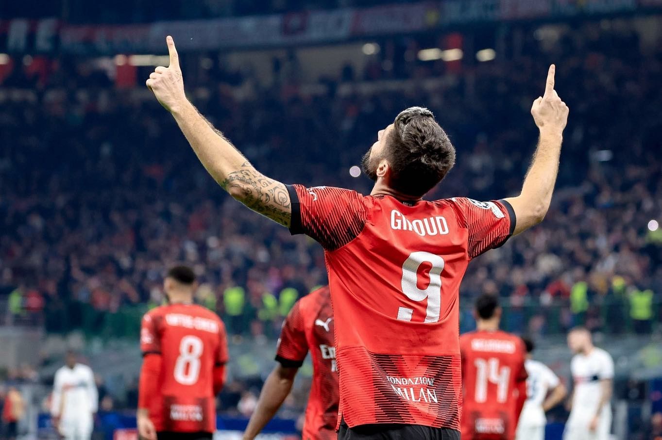 De dos, Olivier Giroud vêtu du maillot de l'AC Milan célèbre son but en pointant ses doigts vers le ciel