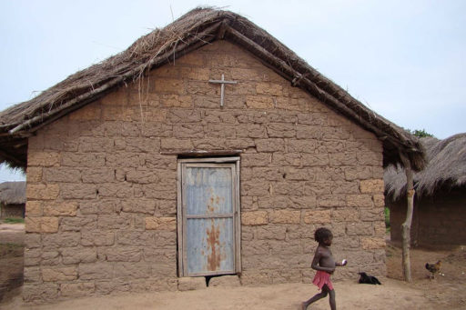 Une petite église rudimentaire en Afrique. Les murs sont en torchis et le toit est en chaume. Il y a une croix sur le mur au-dessus de la porte.