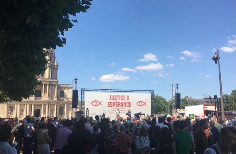 Une foule est amassée dans une avenue de Paris. Au fond se trouve un immense étendard où est écrit: "Justice et espérance,"