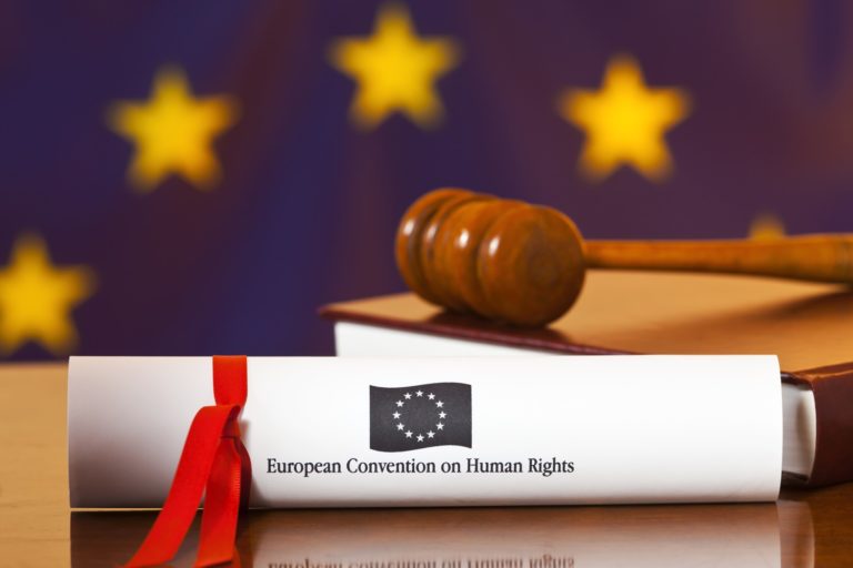 Un marteau de juge posé sur le texte de la Convention européenne des droits de l'homme avec en arrière plan le drapeau de l'Union européenne et ses étoiles jaunes