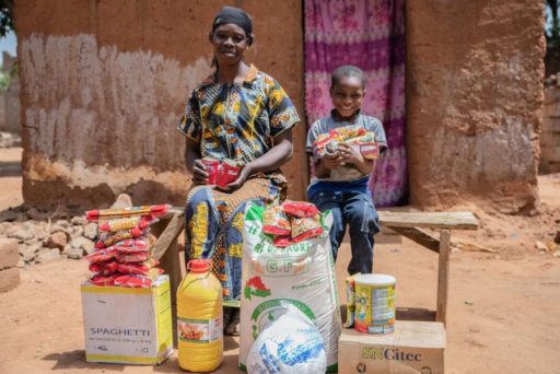 Une mère africaine et son fils, assis sur un banc, sont entourés de provisions