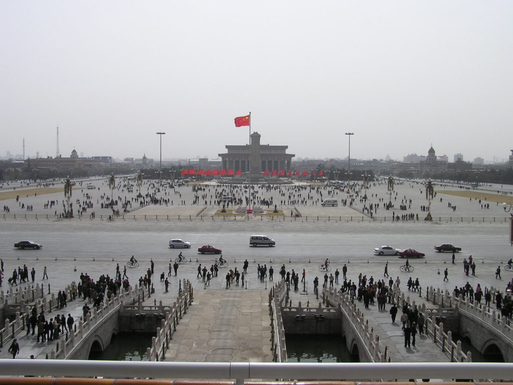 L’immense esplanade de la place Tian'anmen aujourd’hui, avec un drapeau chinois au milieu. Des dizaines de piétons y circulent.