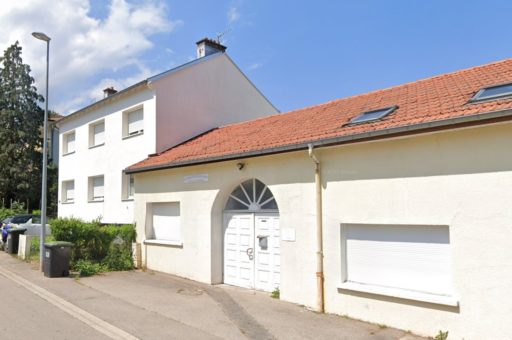 Un bâtiment d'une église évangélique dans un lotissement avec une porte blanche sous un porche et mur mitoyen avec une maison, vue depuis la rue