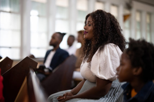 Une dame noire est assise sur un banc d'église, au milieu des autres fidèles. Elle a les yeux fermés et semble profondément heureuse.