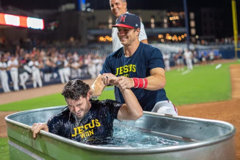 Brewer Hicklen en train de baptiser Wes Clarke dans un abreuvoir à chevaux dans le stade de baseball de Nashville. Les deux hommes portent un T-shirt "Jésus won" (Jésus a gagné)