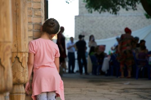 Une jeune fille, cachée derrière un bâtiment observe au loin un groupe d'adultes