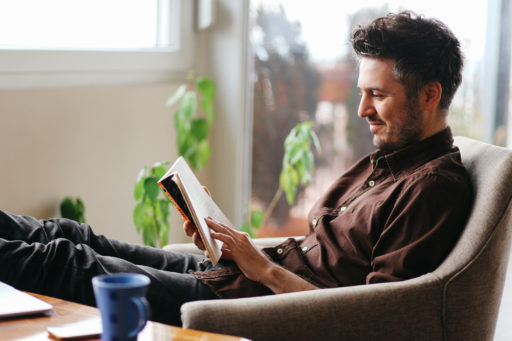 Un homme d'une quarantaine d'année lit un livre dans son salon