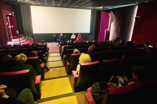 Une salle de cinéma avec un grand écran blanc, des personnes discutent de la projection qui vient d'avoir lieu