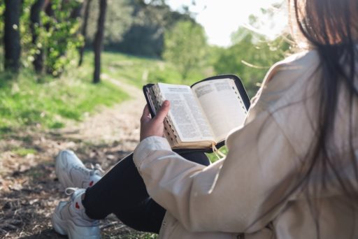 Une femme, assise dans la nature, lit sa Bible