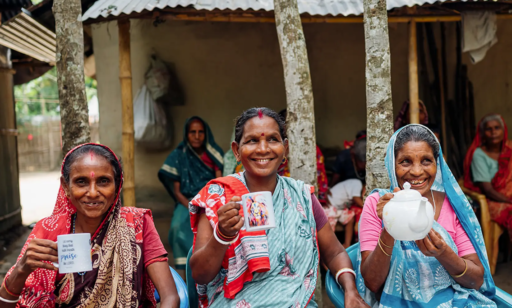 Trois dames indiennes assises lève des tasses et une théière, en signe de célébration. Elles sont très souriantes.